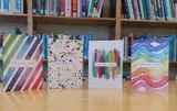 Four colourful thank-you cards standing in front of a bookshelf