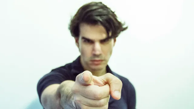A stern-faced man points straight at the camera.