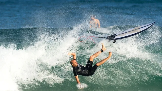 A surfer wiping out off a breaking wave as the board flies clear.