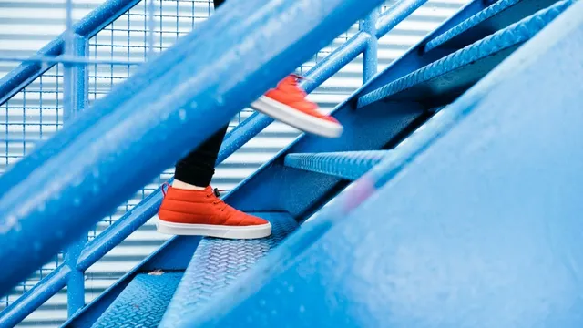 Feet in orange trainers climbing a blue metal staircase.